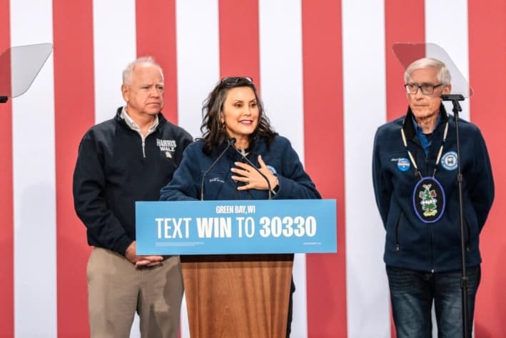 El candidato demócrata a vicepresidente, Tim Walz (izquierda), y el gobernador Tony Evers (D-Wis.) (derecha) escuchan a la gobernadora Gretchen Whitmer (D-Mich.) (centro) hablar en un mitin en el centro de convenciones de KI para dar inicio a su gira "Driving Forward" en Green Bay, Wisconsin, el 14 de octubre de 2024. (Jim Vondruska/Getty Images)
