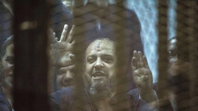 Mohamed el-Beltagy, líder de la Hermandad Musulmana egipcia, muestra el símbolo de los cuatro dedos conocido como “Rabaa” desde detrás de la jaula de los acusados mientras el juez lee la sentencia que lo condena a él y a más de 100 acusados más en la academia de policía de El Cairo, Egipto, el 16 de mayo de 2015. (Khaled Desouki /AFP/Getty Images)
