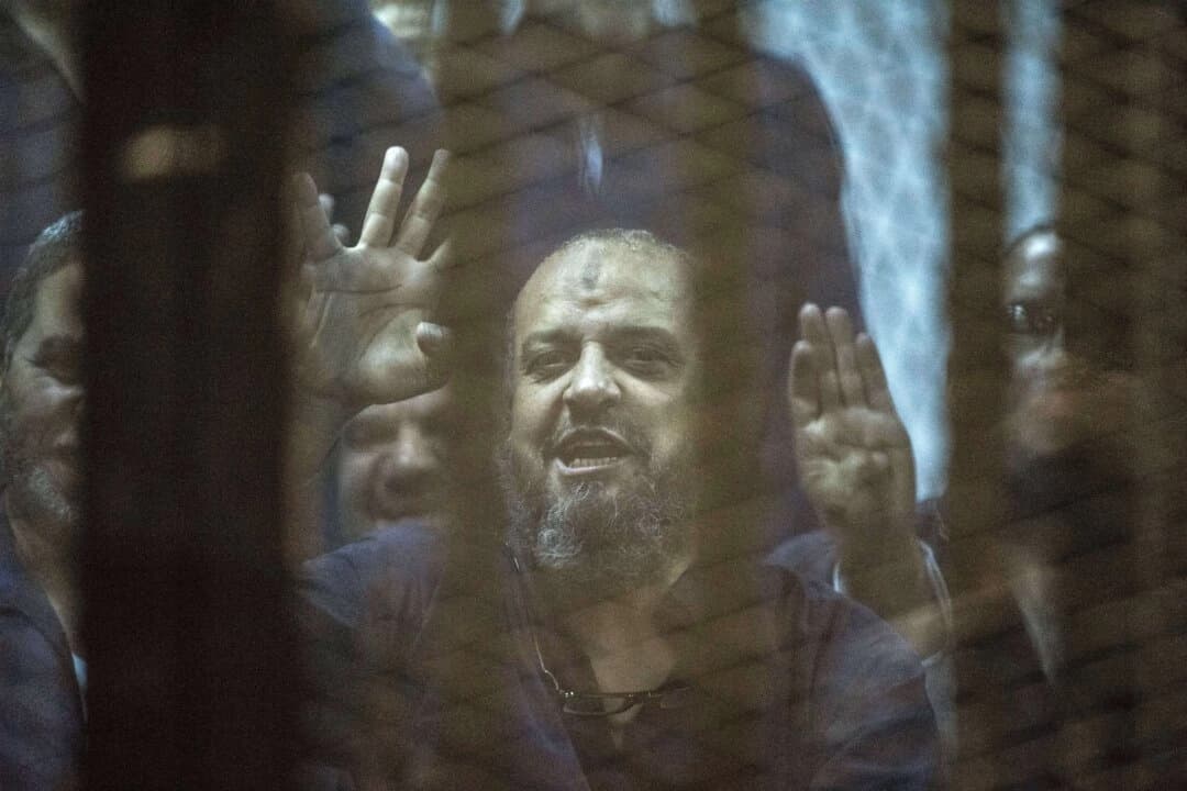Mohamed el-Beltagy, líder de la Hermandad Musulmana egipcia, muestra el símbolo de los cuatro dedos conocido como “Rabaa” desde detrás de la jaula de los acusados mientras el juez lee la sentencia que lo condena a él y a más de 100 acusados más en la academia de policía de El Cairo, Egipto, el 16 de mayo de 2015. (Khaled Desouki /AFP/Getty Images)
