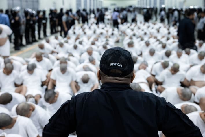 Un guardia vigila a reclusos presuntamente vinculados a organizaciones criminales sentados en el suelo en el Centro de Reclusión Antiterrorista de Tecoluca, El Salvador, el 16 de marzo de 2025. (Gobierno salvadoreño vía Getty Images)