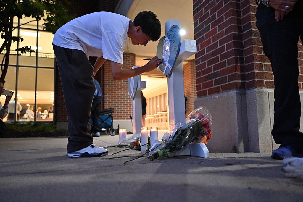 Una persona firma una cruz conmemorativa en una vigilia celebrada en la Academia de los Santos Ángeles de Richfield, Minnesota, en memoria de las víctimas del tiroteo masivo ocurrido en la iglesia y escuela católica Annunciation de Minneapolis, donde dos niños murieron y 17 personas resultaron heridas a manos de un tirador, el 27 de agosto de 2025. (Tom Baker/AFP a través de Getty Images).
