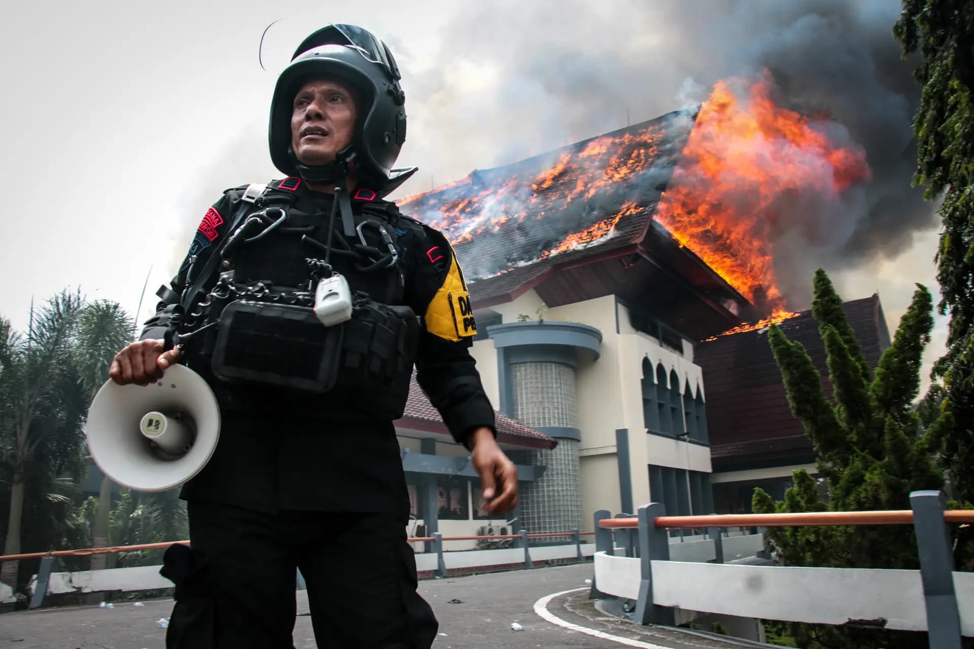 Un oficial de policía sostiene un megáfono mientras el edificio de la oficina del Consejo Provincial de Nusa Tenggara Occidental arde tras ser incendiado por manifestantes en Mataram, isla de Lombok, Nusa Tenggara Occidental, Indonesia, el 30 de agosto de 2025. (Sadim/AFP vía Getty Images)