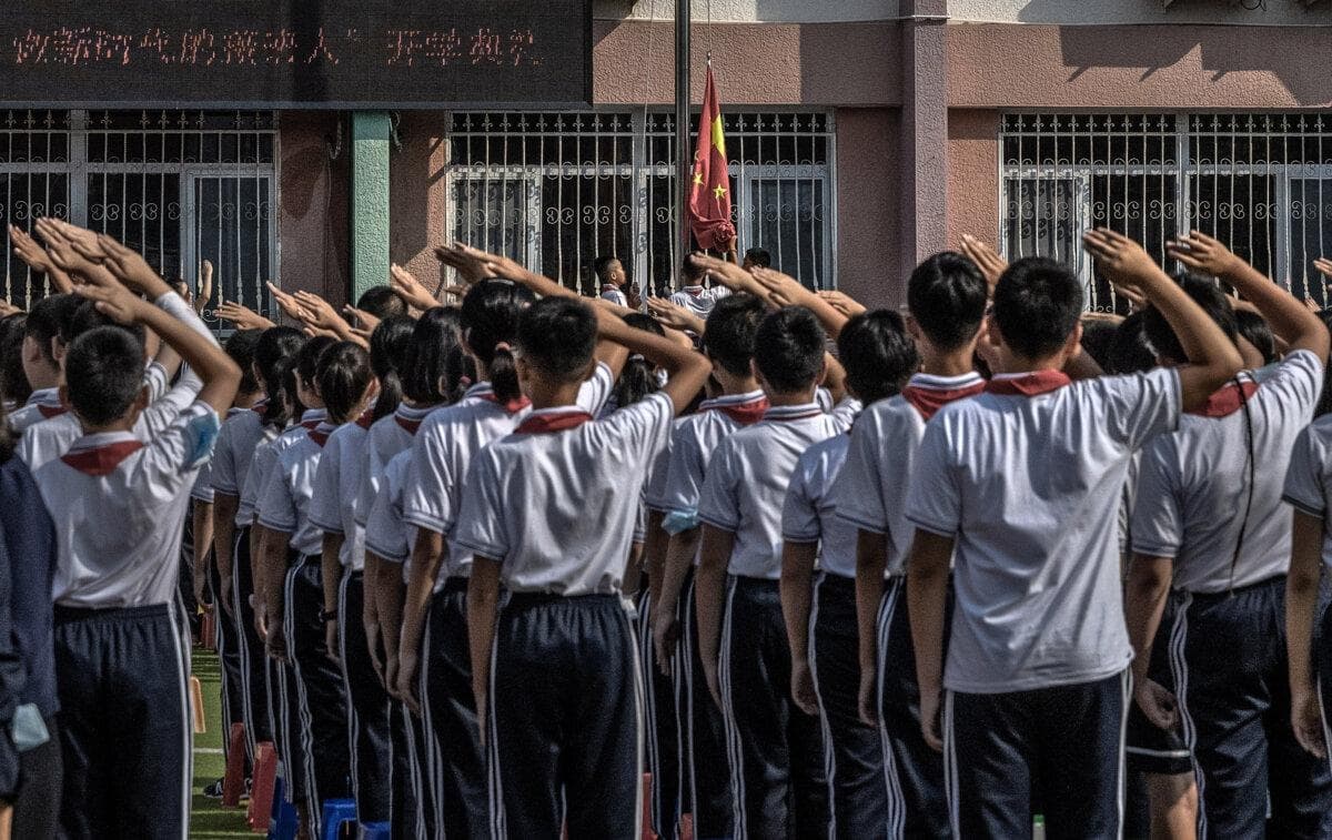 Estudiantes saludan mientras se iza la bandera nacional en una escuela primaria de Beijing el 1 de septiembre de 2021. (Kevin Frayer/Getty Images)