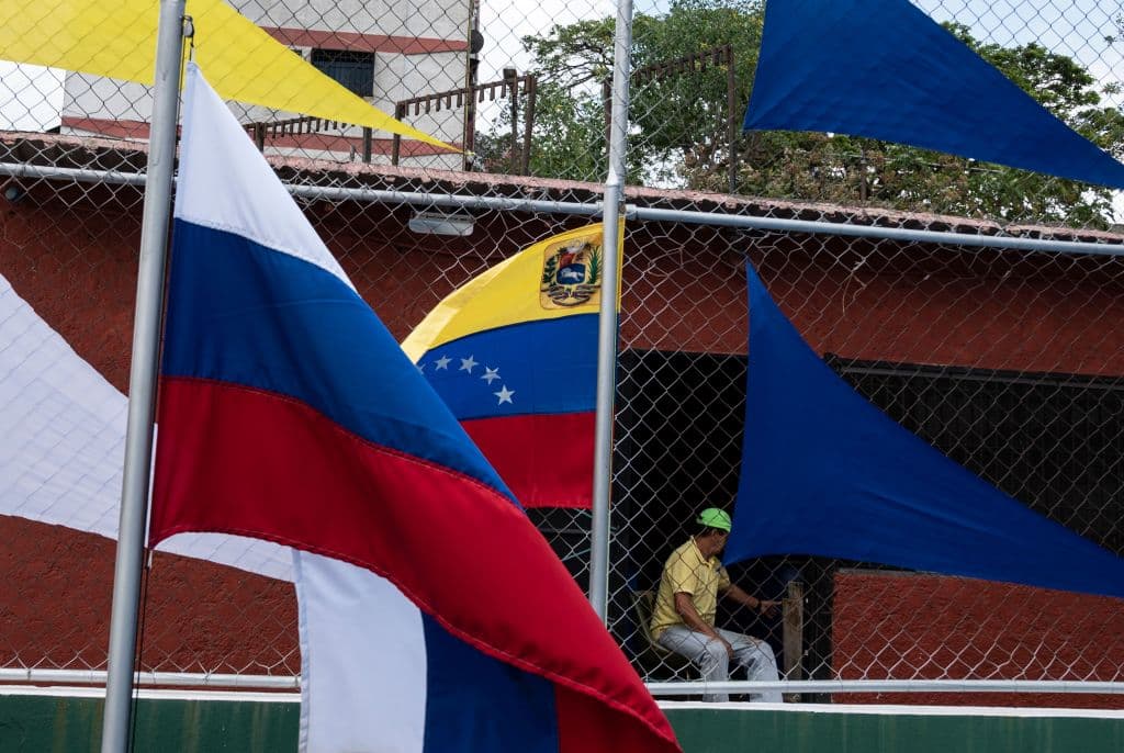 Un hombre sentado frente a las banderas nacionales de Rusia (Izq.) y Venezuela (Dcha.) saluda con la mano en un complejo deportivo recientemente inaugurado en el barrio de Catia, en Caracas, el 4 de abril de 2022. (YURI CORTEZ/AFP vía Getty Images)
