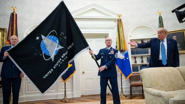 El general John "Jay" Raymond, comandante del Comando Espacial de Estados Unidos (izquierda), y el sargento mayor Roger Towberman (derecha) sostienen la bandera mientras el presidente Donald Trump hace un gesto, durante la presentación de la bandera de la Fuerza Espacial en el Despacho Oval de la Casa Blanca en Washington, el 15 de mayo de 2020. (AP/Alex Brandon, archivo)
