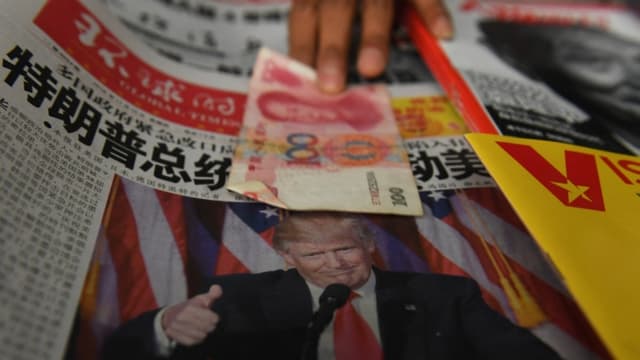 Foto ilustrativa: Un vendedor recoge un billete de 100 yuanes sobre un periódico que muestra una foto del presidente electo de Estados Unidos, Donald Trump, en un puesto de periódicos en Beijing el 10 de noviembre de 2016. (GREG BAKER/AFP via Getty Images)