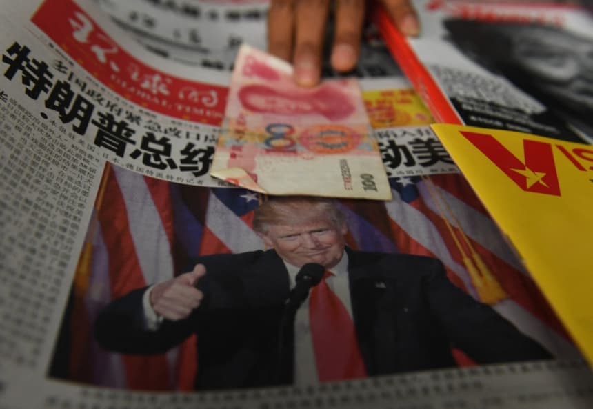 Foto ilustrativa: Un vendedor recoge un billete de 100 yuanes sobre un periódico que muestra una foto del presidente electo de Estados Unidos, Donald Trump, en un puesto de periódicos en Beijing el 10 de noviembre de 2016. (GREG BAKER/AFP via Getty Images)