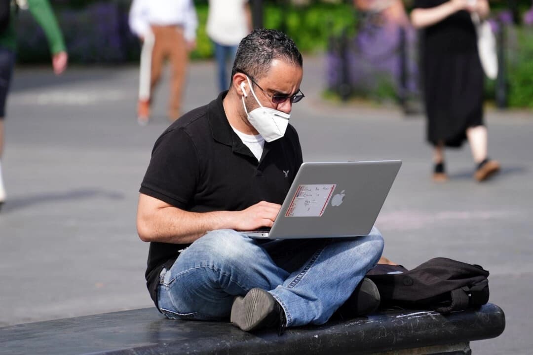 Un hombre con mascarilla usa una computadora portátil en una foto de archivo. (Cindy Ord/Getty Images)
