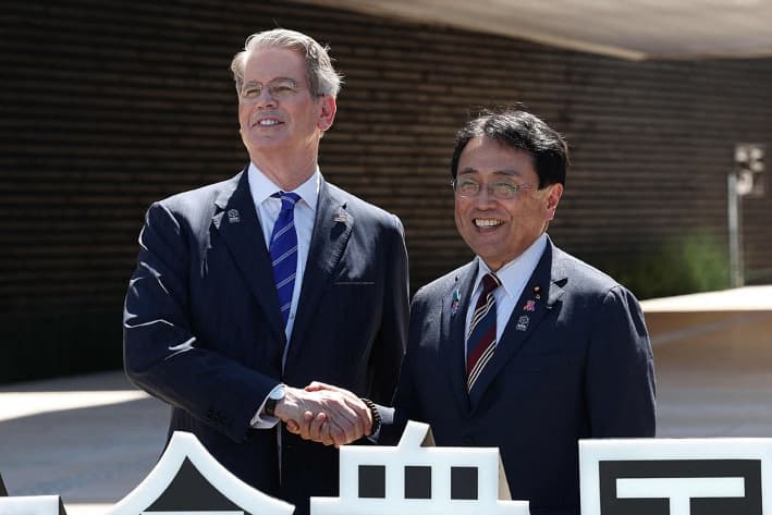 El secretario del Tesoro de Estados Unidos, Scott Bessent (izq.), estrecha la mano del ministro de revitalización económica de Japón y negociador jefe en las negociaciones arancelarias, Ryosei Akazawa (der.), frente al pabellón estadounidense en la Expo de Osaka mientras asisten a las celebraciones del día nacional de Estados Unidos, en la ciudad de Osaka, el 19 de julio de 2025. (STR/JIJI Press/AFP vía Getty Images)