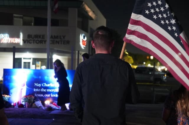 Un hombre con una bandera estadounidense en la mano posa delante de una pancarta iluminada en honor al fundador de Turning Point USA, Charlie Kirk, asesinado en Phoenix, Arizona, el 10 de septiembre de 2025. Allan Stein/The Epoch Times