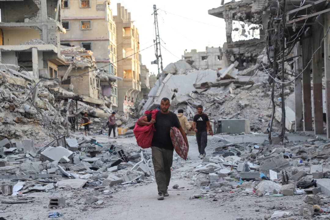 Palestinos caminan cerca de los escombros tras una ofensiva israelí llevada a cabo antes de que se alcanzara un alto al fuego entre Israel y Hamás, en el campo de refugiados de Shati, en la ciudad de Gaza, el 12 de octubre de 2025. (Ebrahim Hajjaj/Reuters)