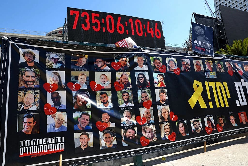 Retratos de los rehenes israelíes retenidos en la Franja de Gaza desde los ataques del 7 de octubre de 2023 se exhiben bajo un reloj digital que muestra los días, horas y minutos que llevan cautivos, frente al Museo de Arte de Tel Aviv, conocido como "Plaza de los Rehenes", en Tel Aviv, Israel, el 11 de octubre de 2025. (Jack Guez/AFP a través de Getty Images).