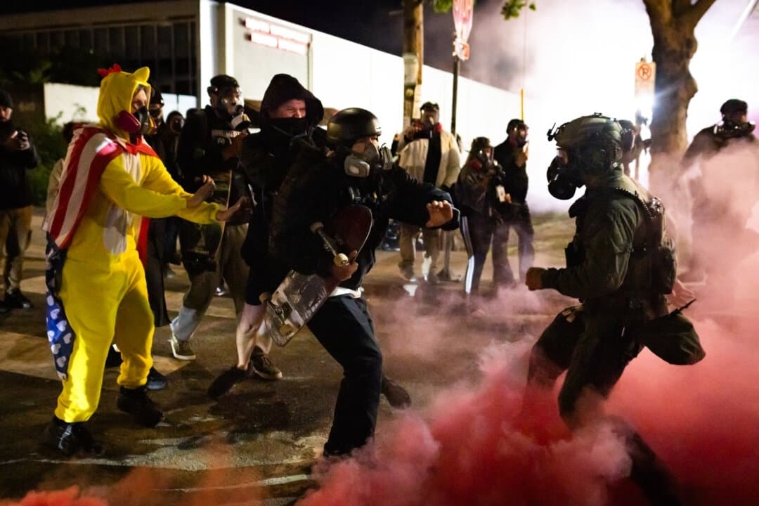 Un manifestante violento devuelve una bomba de humo lanzada por agentes federales en su dirección frente a las oficinas del Servicio de Inmigración y Control de Aduanas en Portland, Oregón, el 5 de octubre de 2025. (John Fredricks/The Epoch Times)
