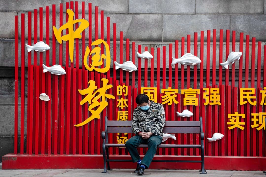 Un residente con mascarilla toma una siesta en un banco cerca del eslogan propagandístico del PCCh "Sueño chino" en Wuhan, China, el 1 de abril de 2020. (Ng Han Guan/Foto AP)