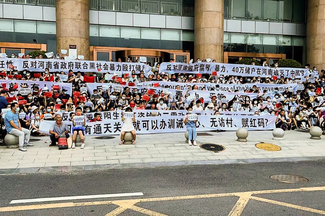La gente sostiene pancartas y corea consignas durante una protesta a la entrada de una sucursal del banco central chino en Zhengzhou, en la provincia central de Henan, China, el 10 de julio de 2022. Cuatro bancos rurales de la provincia dejaron de permitir a los clientes retirar efectivo desde abril de 2022. (Yang/AP Photo)