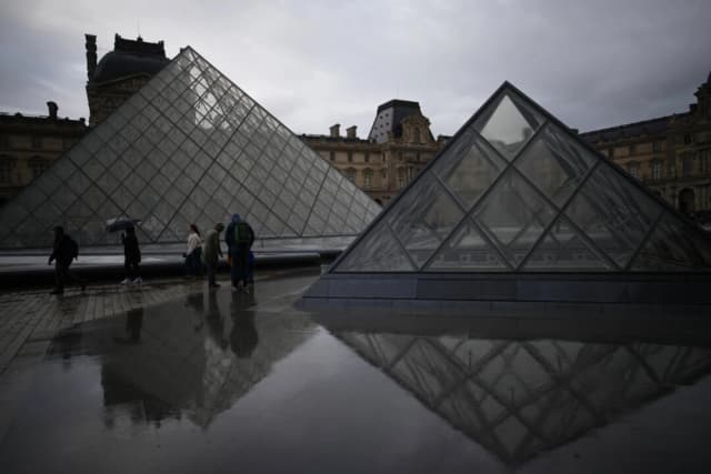 Visitantes recorren el patio del museo del Louvre bajo la lluvia en París, el 27 de octubre de 2025. (Foto: Christophe Ena/AP)