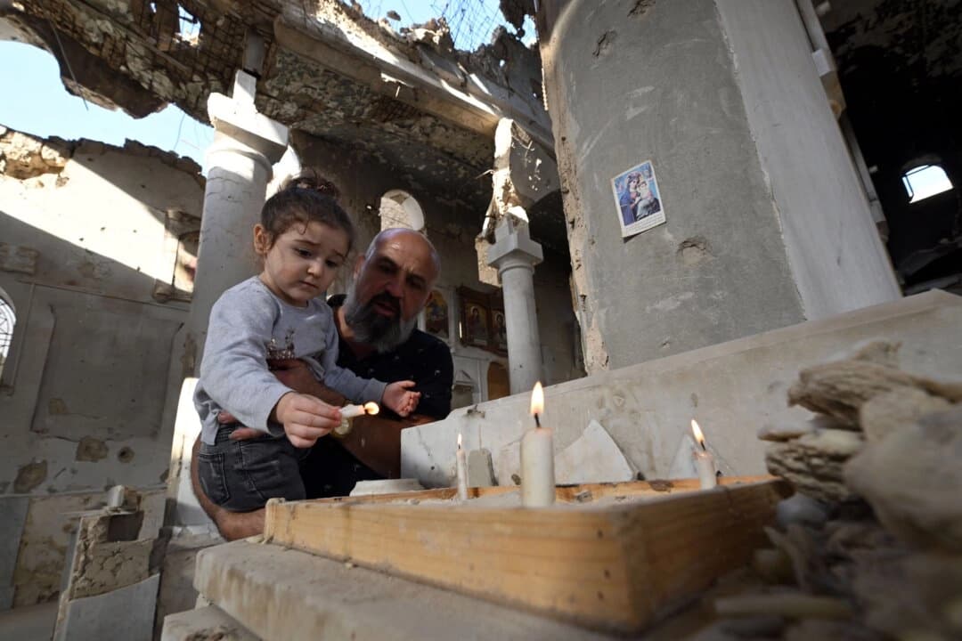 Un cristiano sostiene a su hija mientras encienden velas en el altar de la iglesia ortodoxa griega de Saint Takla, en Darayya, a las afueras de Damasco, el 28 de octubre de 2025, mientras Siria se enfrenta a uno de sus retos más importantes: la reconstrucción bajo el nuevo liderazgo tras el derrocamiento del gobernante baazista Bashar al-Assad el pasado mes de diciembre. (Louai Beshara/AFP).