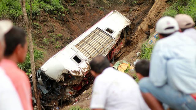 La gente observa los restos de un autobús que cayó a un profundo barranco al descender cerca de La Crespa, cuando viajaba desde la capital, Quito, hacia las localidades orientales de Chone y San Isidro, el 24 de diciembre de 2010.  (Rodolfo Parraga/AFP a través de Getty Images).