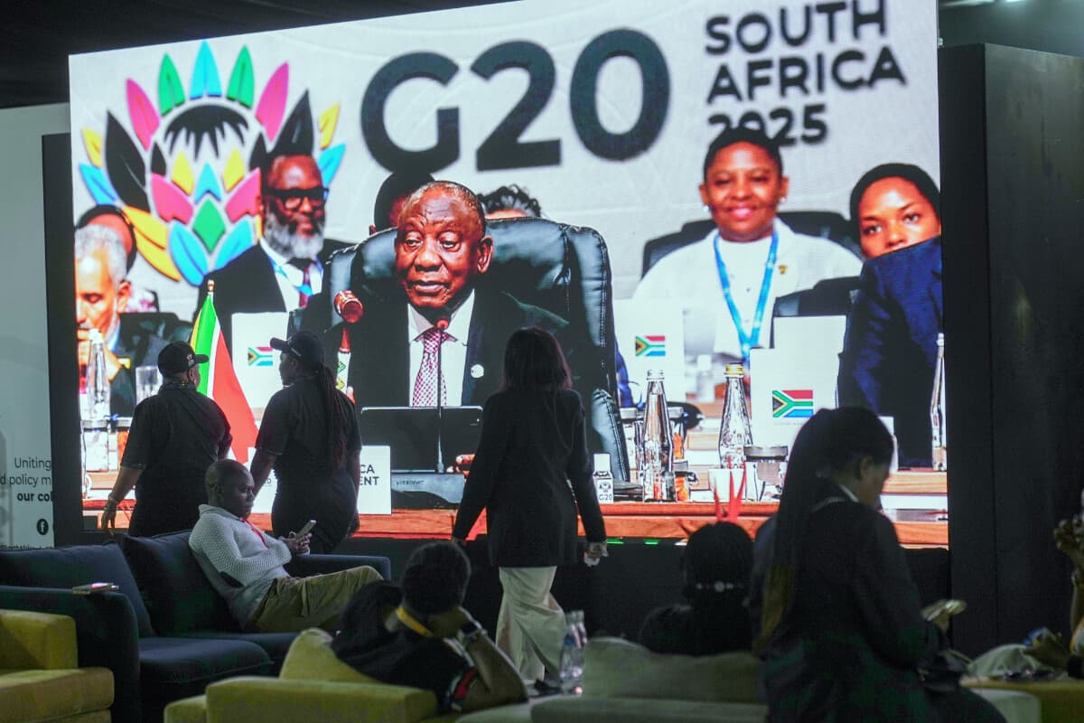 La gente pasa junto a una gran pantalla de televisión en la que se ve al presidente sudafricano Cyril Ramaphosa sosteniendo un mazo de madera mientras clausura oficialmente la cumbre de líderes del G20, en Johannesburgo, Sudáfrica, el 23 de noviembre de 2025. (Jerome Delay/AP Photo).