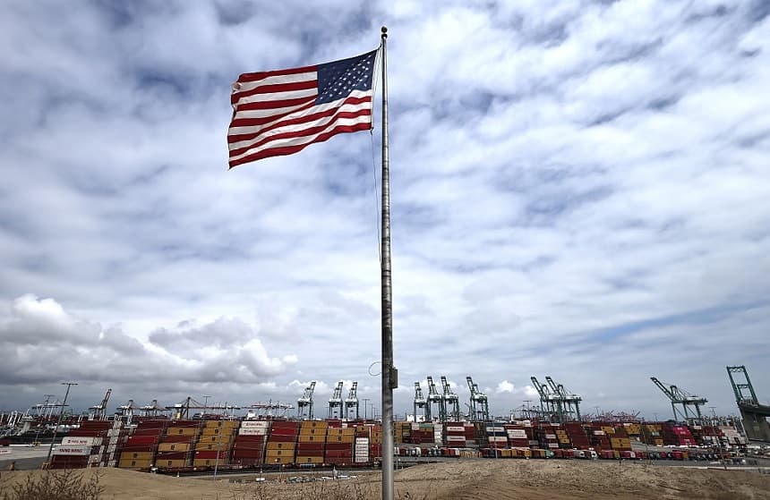 Una bandera estadounidense ondea frente a contenedores de transporte y grúas en el puerto de Los Ángeles el 26 de septiembre de 2025 en Los Ángeles, California. (Mario Tama/Getty Images)