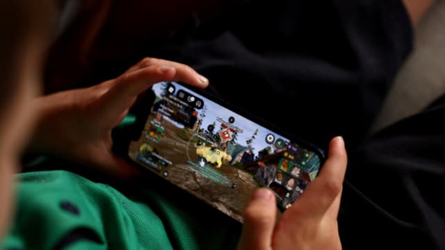  En esta ilustración fotográfica, unos niños pequeños sostienen un iPhone mientras utilizan la plataforma de juegos online Roblox el 19 de noviembre de 2025 en Auckland, Nueva Zelanda. (Ilustración fotográfica de Getty Images)