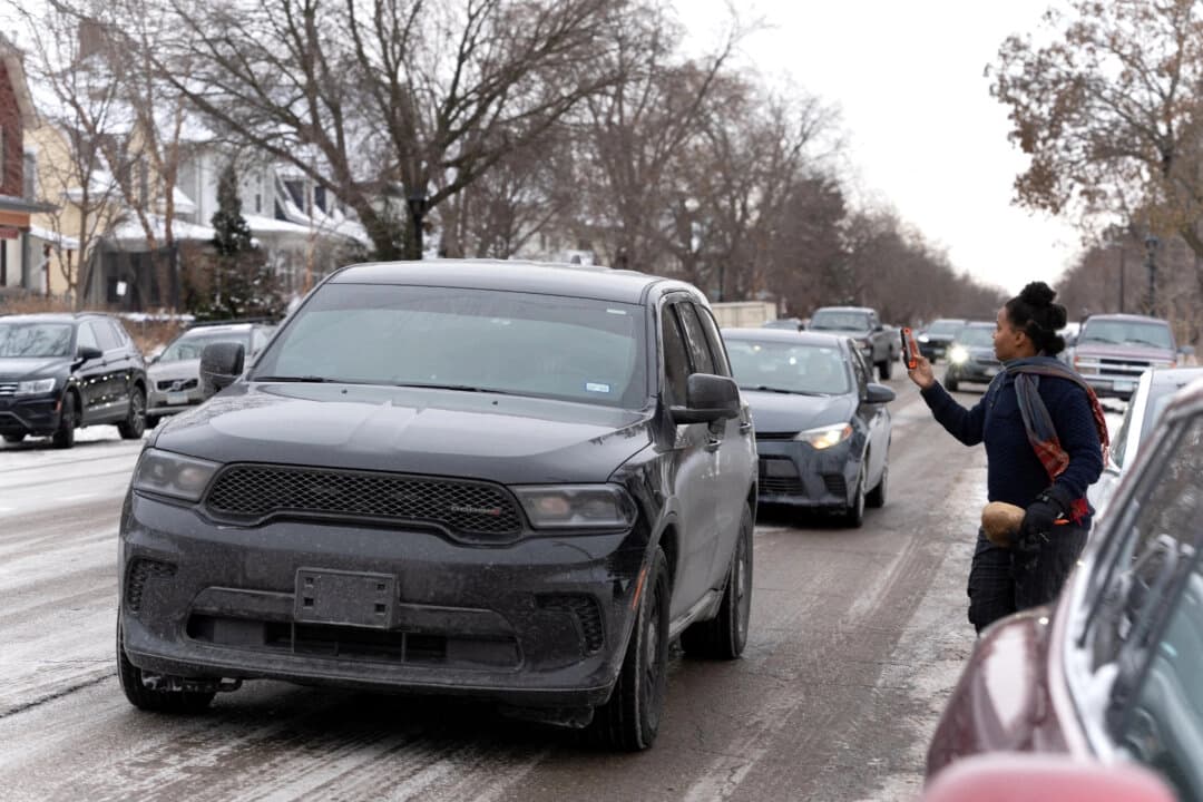 Una observadora comunitaria de respuesta rápida sostiene su teléfono mientras un vehículo que transporta a agentes federales pasa por delante durante una redada de inmigración en una vivienda de la zona sur de Minneapolis el 4 de diciembre de 2025. (Tim Evans/Reuters)