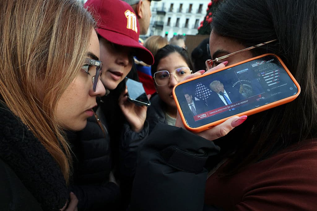 Venezolanos en España siguen con sus teléfonos inteligentes la conferencia de prensa del presidente estadounidense Donald Trump, reunidos en la Puerta del Sol de Madrid el 3 de enero de 2026, después de que las fuerzas estadounidenses capturaran al líder venezolano Nicolás Maduro tras lanzar un "ataque a gran escala" contra Venezuela. (Foto de Pierre-Philippe MARCOU / AFP vía Getty Images)