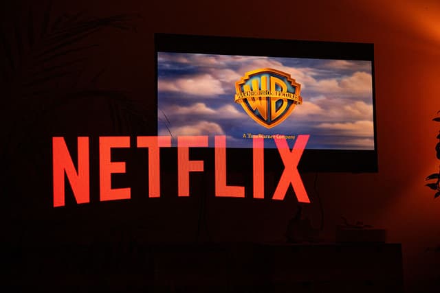 Fotografía de doble exposición del logotipo de Netflix y el logotipo de Warner Bros en una pantalla de televisión en Kerlouan, en Bretaña, Francia, el 5 de diciembre de 2025. (Foto de Vincent Feuray / Hans Lucas / AFP a través de Getty Images)
