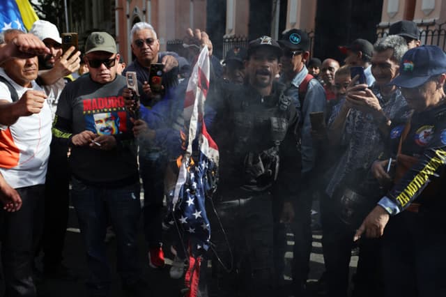 Miembros de la fuerza Colectivo y partidarios de Nicolás Maduro queman una bandera de Estados Unidos durante una concentración cerca del palacio de Miraflores tras escucharse explosiones y aviones volando a baja altura en la madrugada del 3 de enero de 2026 en Caracas, Venezuela. (Jesús Vargas/Getty Images)