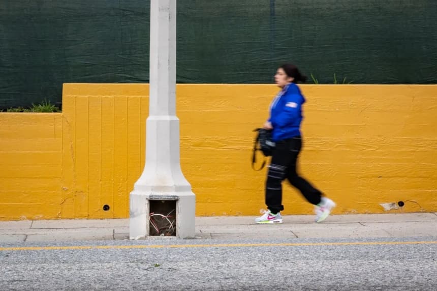 Una mujer pasa junto a una farola que fue objeto de un robo de cables en Los Ángeles, el 4 de abril de 2024. (John Fredricks/The Epoch Times)