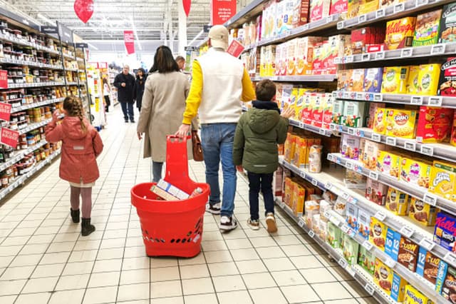 Dos padres y sus dos hijos caminan por una sección de pasteles, galletas y mermeladas, con el padre tirando de una cesta llena de artículos, en el supermercado Auchan de Guilherand Granges, Francia, el 1 de febrero de 2025. (Foto de Nicolas Guyonnet / Hans Lucas/AFP vía Getty Images).