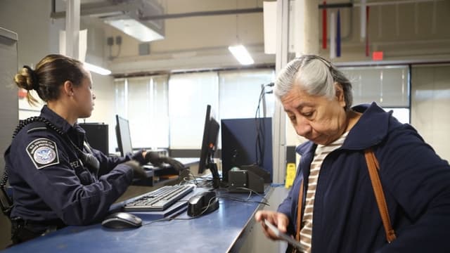 Una oficial de Aduanas y Protección Fronteriza de los Estados Unidos espera a un migrante después de revisar los documentos de una mujer que ingresa a Estados Unidos por el puerto de entrada de San Ysidro el 9 de abril de 2018 en San Ysidro, California. (Mario Tama/Getty Images)