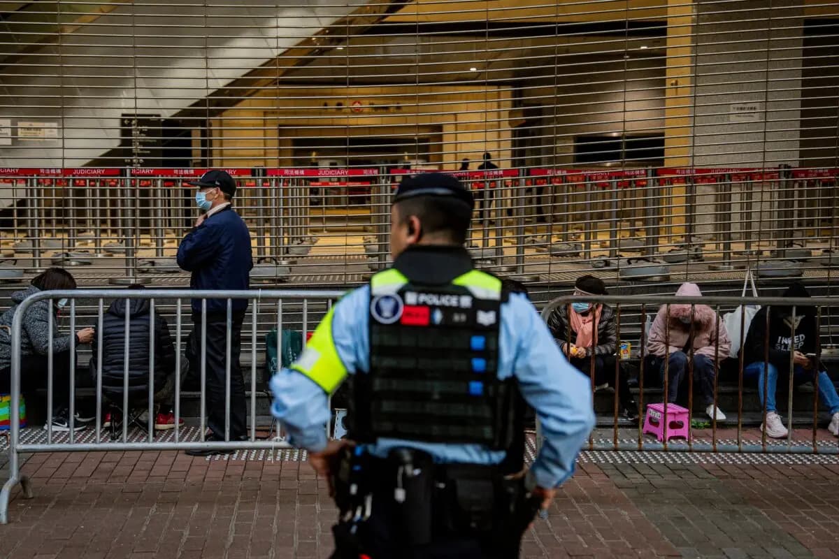 Un policía vigila a gente en una fila antes de entrar al edificio de los Tribunales de West Kowloon para escuchar los veredictos en el juicio de seguridad nacional del magnate de los medios prodemocracia Jimmy Lai en Hong Kong el 15 de diciembre de 2025. (Leung Man Hei/AFP vía Getty Images)
