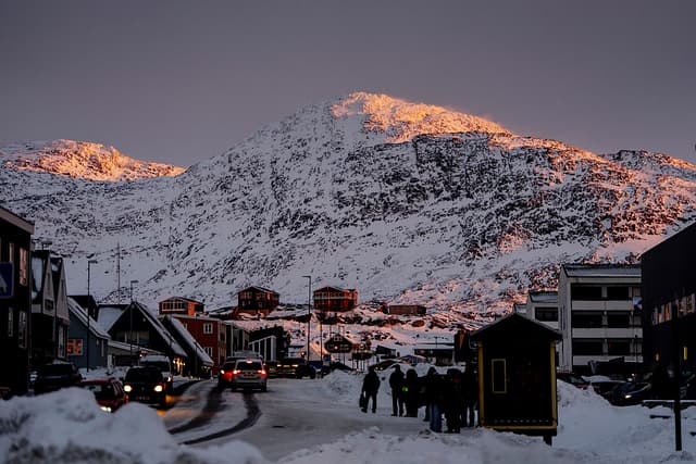 Un punto de luz cálida ilumina la cima de una colina cubierta de nieve, mientras se ven coches y personas a lo largo de una carretera al atardecer en Nuuk, Groenlandia, el 21 de enero de 2026. (Foto de Mads Claus Rasmussen / Ritzau Scanpix / AFP a través de Getty Images) / Dinamarca OUT)