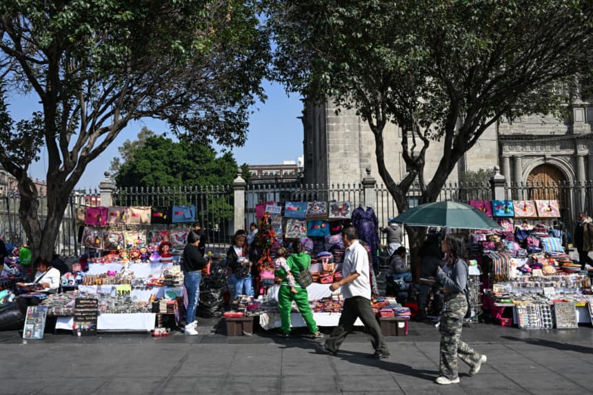 Personas caminan frente a artesanías y otros artículos a la venta en puestos callejeros en la Plaza de la Constitución, conocida como El Zócalo, en la Ciudad de México, el 9 de diciembre de 2025. (Yuri CORTEZ/AFP vía Getty Images)