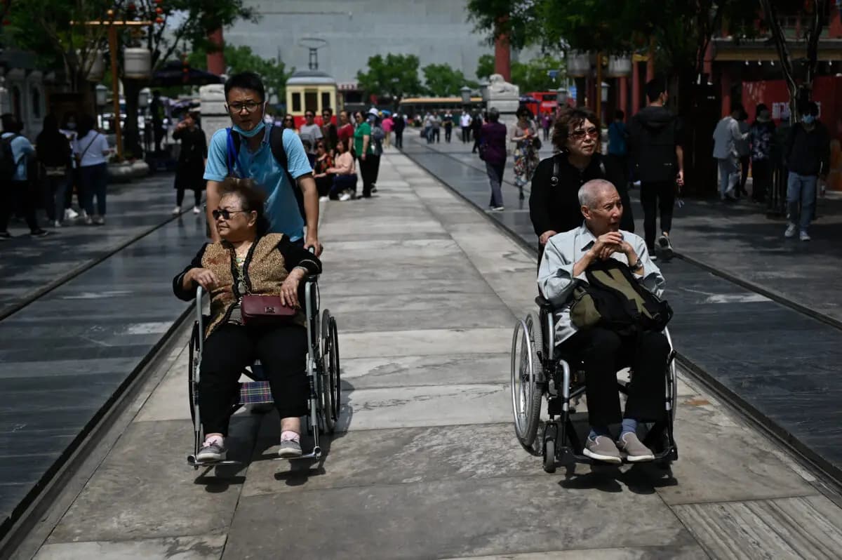 Un anciano y una anciana son empujados en sillas de ruedas por una calle de Pekín el 11 de mayo de 2021. (Wang Zhao/AFP vía Getty Images)