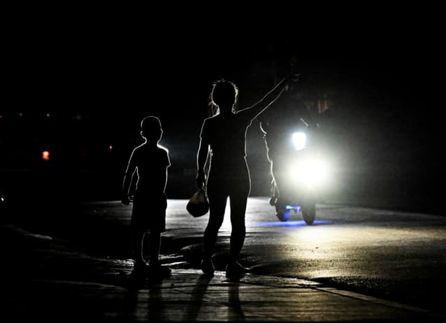 Una mujer con su hijo le hace señas a un auto en una calle oscura durante un apagón en el municipio de Bauta, provincia de Artemisa, Cuba, el 18 de marzo de 2024. (YAMIL LAGE/AFP via Getty Images)