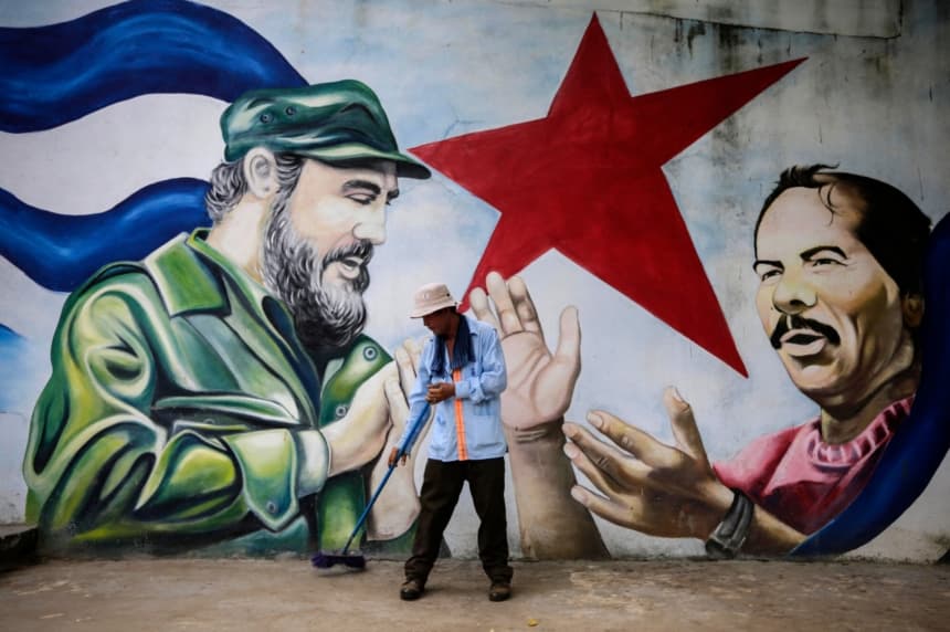 Imagen ilustrativa: Un trabajador municipal barre el suelo frente a un mural que representa al líder revolucionario cubano Fidel Castro (izq.) y al presidente nicaragüense Daniel Ortega en la Plaza Cuba de Managua, el 26 de noviembre de 2016, al día siguiente de la muerte de Castro. (INTI OCON/AFP via Getty Images)