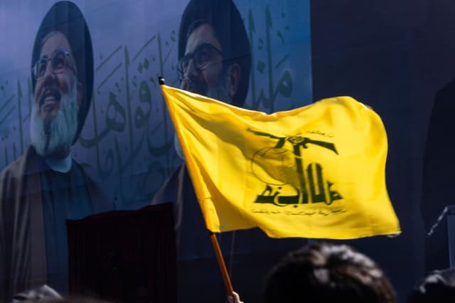 Una bandera de Hezbolá ondea frente a una ilustración de los antiguos líderes de Hezbolá, Hassan Nasrallah, a la izquierda, y Hashem Safieddine, en el escenario de sus funerales en el Estadio Sports City el 23 de febrero de 2025 en Beirut, Líbano. (Daniel Carde/Getty Images)