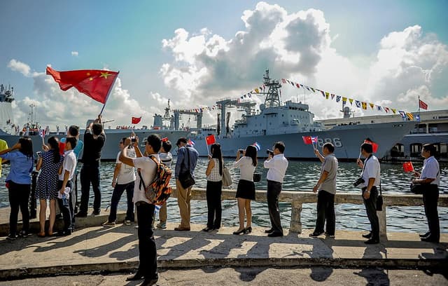Personas ondean banderas cubanas y de la República Popular China mientras varios buques de la Armada china ingresan al puerto de La Habana el 10 de noviembre de 2015. (YAMIL LAGE/AFP vía Getty Images)