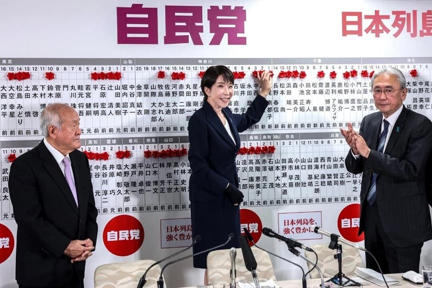 La primera ministra japonesa y presidenta del Partido Liberal Democrático (PLD), Sanae Takaichi (C), junto al secretario general del PLD, Shunichi Suzuki (I), y el jefe de estrategia electoral del PLD, Keiji Furuya, coloca una rosa de papel roja sobre el nombre de un candidato elegido en la sede del PLD durante las elecciones a la Cámara de Representantes en Tokio el 8 de febrero de 2026. (Kim Kyung-Hoon/Pool/AFP/Getty Images)
