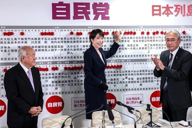 La primera ministra japonesa y presidenta del Partido Liberal Democrático (PLD), Sanae Takaichi (C), junto al secretario general del PLD, Shunichi Suzuki (I), y el jefe de estrategia electoral del PLD, Keiji Furuya, coloca una rosa de papel roja sobre el nombre de un candidato elegido en la sede del PLD durante las elecciones a la Cámara de Representantes en Tokio el 8 de febrero de 2026. (Kim Kyung-Hoon/Pool/AFP/Getty Images)
