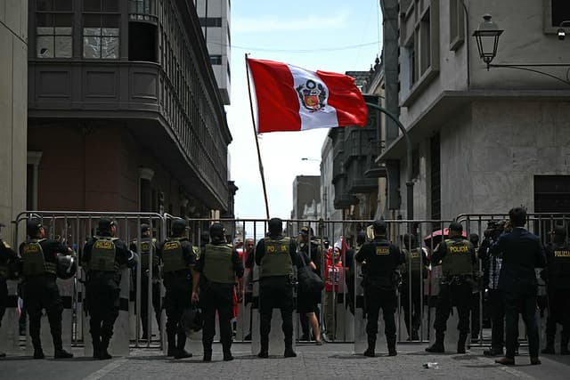 Policías vigilan mientras la gente protesta con una bandera peruana frente al edificio Faustino Sánchez Carrión, del poder legislativo, donde el Congreso peruano considerará si destituirá al presidente interino José Jeri, en Lima, el 17 de febrero de 2026. Jeri, el séptimo jefe de Estado en 10 años, está acusado de la contratación irregular de varias mujeres en su gobierno, y una moción para destituirlo por tráfico de influencias recibió el respaldo de decenas de legisladores. (Foto de ERNESTO BENAVIDES / AFP vía Getty Images)