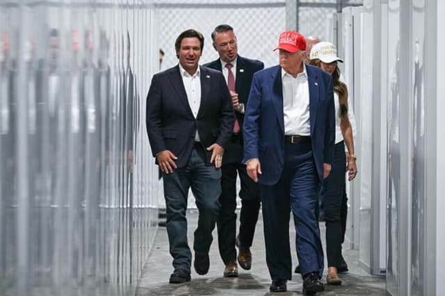 El presidente de los Estados Unidos, Donald Trump (segundo por la derecha), el gobernador de Florida, Ron DeSantis (izquierda), y la secretaria de Seguridad Nacional, Kristi Noem (derecha), recorren una sección de instalaciones médicas durante su visita a un centro de detención de migrantes, apodado "Alligator Alcatraz", ubicado en el aeropuerto de entrenamiento y transición Dade-Collier en Ochopee, Florida, el 1 de julio de 2025.  (ANDREW CABALLERO-REYNOLDS/AFP vía Getty Images).