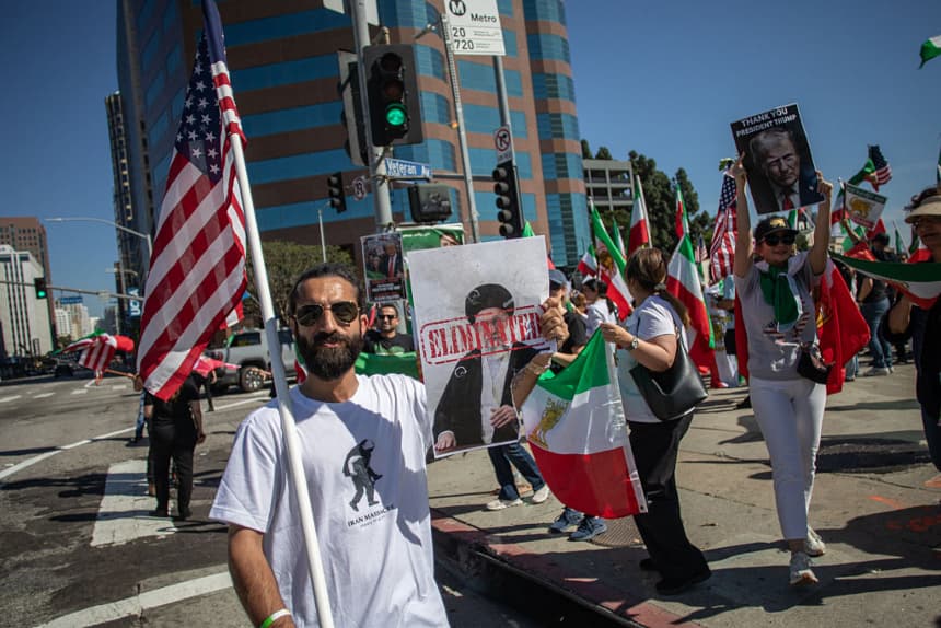 Un hombre sostiene una bandera estadounidense y un cartel con el retrato del líder supremo iraní, el ayatolá Alí Jamenei, que dice "eliminado", mientras miembros de la comunidad iraní celebran frente al Edificio Federal en el barrio West LA de Los Ángeles, el 28 de febrero de 2026. (Apu GOMES/AFP vía Getty Images)