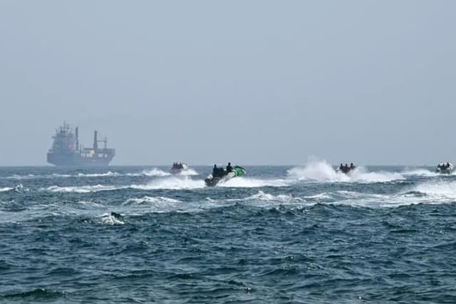 Pequeñas embarcaciones cargadas de mercancías navegan junto al buque portacontenedores Marsa Victory, con bandera de San Cristóbal y Nieves, en las aguas del estrecho de Ormuz, frente a la costa de Khasab, en la península de Musandam, al norte de Omán, el 25 de junio de 2025. (GIUSEPPE CACACE/AFP a través de Getty Images).