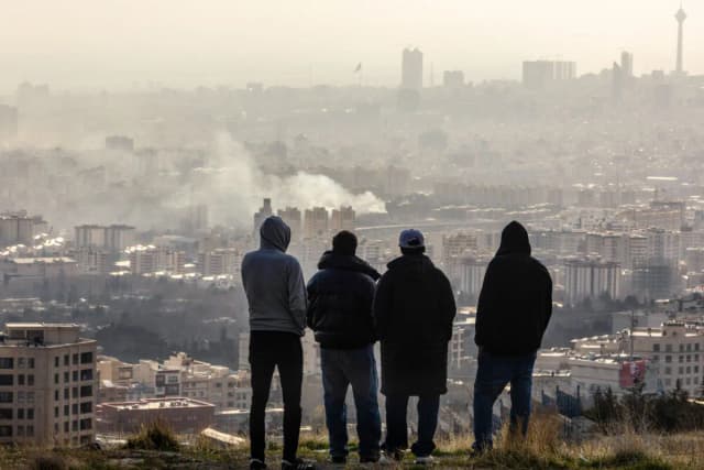 Hombres observan desde una ladera cómo se eleva una columna de humo tras una explosión en Teherán, Irán, el 2 de marzo de 2026. (Majid Saeedi/Getty Images)