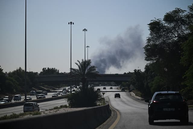 Conductores circulan por una calle mientras el humo se eleva tras un supuesto ataque iraní en la zona donde se encuentra la embajada de Estados Unidos en la ciudad de Kuwait, el 2 de marzo de 2026. (Foto de AFP vía Getty Images)