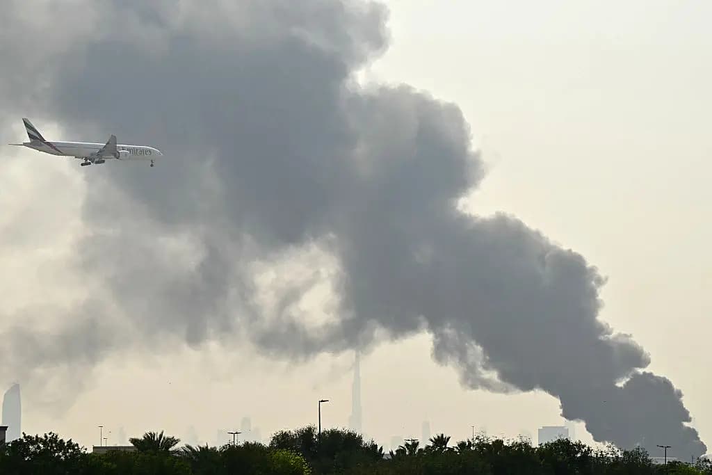 Un avión de Emirates sobrevuela las columnas de humo de un incendio cerca del Aeropuerto Internacional de Dubái, en Dubái (Emiratos Árabes Unidos), el 16 de marzo de 2026. (AFP vía Getty Images).
