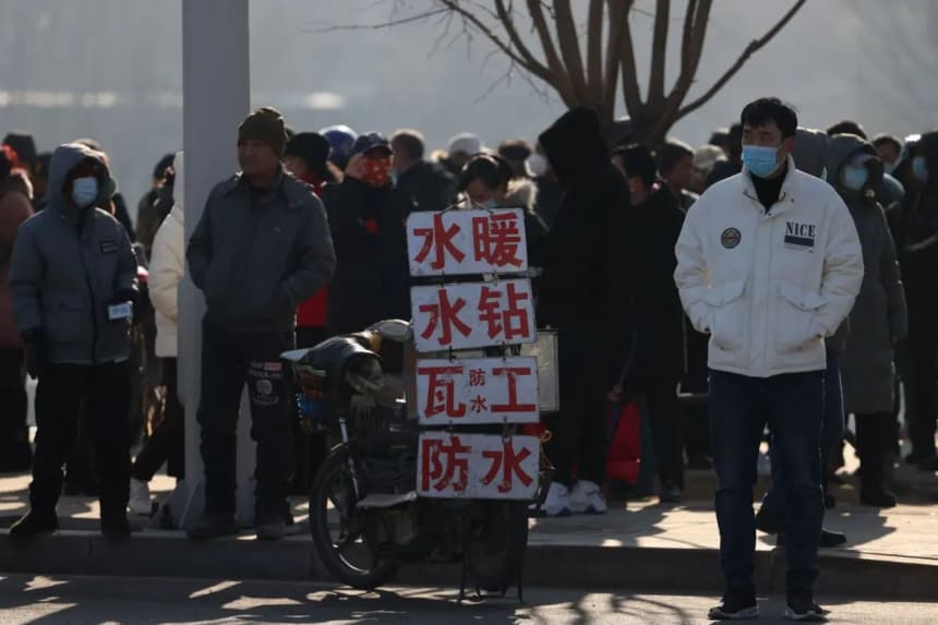 Trabajadores migrantes junto a carteles en los que anuncian sus habilidades mientras esperan ser contratados en Shenyang, en la provincia de Liaoning, al noreste de China, el 6 de febrero de 2023. (AFP vía Getty Images)